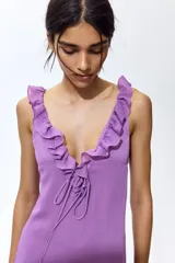 Vestido midi color lila, de corte recto, con escote en V profundo decorado con volados y tiras finas para anudar.