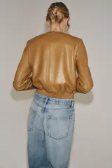 Campera bomber de cuero 100% color tostado de la ZARA WOMAN COLLECTION, con cuello redondo, manga larga, bolsillos delanteros ribeteados y cierre frontal con botones metálicos en relieve. Presenta elástico fruncido en el dobladillo inferior.