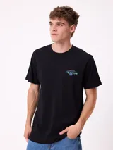 Remera de manga corta color blanco con estampa gráfica en la espalda en color azul, que presenta un diseño de estilo surf con una camioneta, un pelícano y texto alusivo a la marca Rusty.