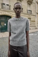 Jersey de cuello redondo color gris, con abalorios joya en el cuello, manga corta y tejido efecto cepillado. Cierre en la espalda con abertura y botón.