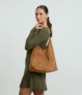 Cartera tipo hobo de gran tamaño confeccionada en material sintético efecto gamuza color tostado. Presenta una estructura flexible, asa única en tono contrastante y cierre mediante botón a presión.