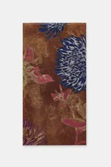 Pañuelo rectangular de gran tamaño con estampado floral de peonías en tonos azules y rosados sobre fondo marrón. Presenta bordes con acabado deshilachado.