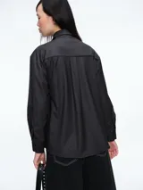 Camisa de corte clásico en color gris oscuro, con cuello camisero, mangas largas con puños abotonados y cierre frontal con botones. Incluye una corbata a tono con un broche decorativo en forma de flor metálica en el cuello.