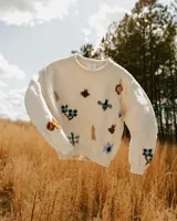 Sweater de punto jersey de lana merino en color marfil, con cuello redondo y bordados artesanales a mano de insectos y flores multicolores en el frente y las mangas.