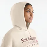 Canguro New Balance de felpa francesa color beige, con capucha ajustable, bolsillo estilo canguro y diseño extragrande. Presenta el logotipo bordado en el pecho en tonos bordó y rosa.
