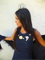 Vestido largo de crochet en color azul marino, con diseño sin mangas y cuello redondo. Presenta un detalle de apliques metálicos en la zona del pecho y un ruedo con volado de textura contrastante.