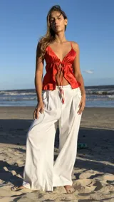 Top de satén color rojo vibrante, con escote pronunciado en V y lazos finos para atar en el frente y en la espalda. Presenta un diseño fruncido en la parte inferior.