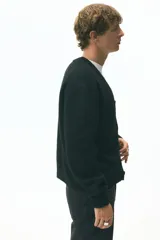 Cárdigan negro de punto peludo suave, con cuello en V pronunciado y cierre frontal de botones. Presenta remates acanalados en puños y bajo.