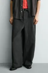 Pantalón de corte relajado confeccionado en tejido de algodón. Presenta cintura con trabillas laterales ajustables, bolsillos frontales y traseros, y un diseño distintivo de costuras laterales giradas que recorren la pernera.