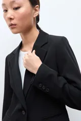 Blazer clásico de corte entallado, color negro, con cierre frontal de un botón, solapas de muesca y bolsillos laterales con solapa.