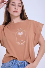 Remera color camel de algodón con mangas cortas con efecto de hombrera y estampado con una palmera y la frase "Welcome to La Guia Summer Vacation".