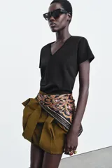 Cinturón tipo pañuelo de tejido satinado con estampado paisley en tonos rojos, azules, verdes y dorados sobre fondo negro. Presenta cierre con hebilla metálica y aplicación de tiras de piel.