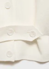 Cardigan de punto acanalado color blanco, con cuello en pico, manga larga y cierre frontal de botones. Presenta un diseño recto con una tira decorativa ajustable en la cintura con botones.