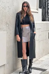 Tapado largo de cuero negro con cuello desmontable y detalles en peltre en las mangas. El cuello desmontable es reversible, de un lado peltre y del otro marrón.