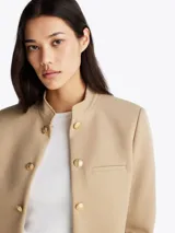 Americana beige de corte slim con cuello mao, cierre de gancho oculto, bolsillo de ojal en el pecho, totalmente forrada y logo esmaltado de Tommy Hilfiger en el puño.