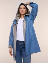 Pilot engomado impermeable color azul, de corte recto estilo trench con acabado resistente al agua. Cuenta con capucha integrada, cierre frontal con broches a presión, bolsillos laterales con ojal y forro interior de tela estampada a cuadros visible en la solapa y los puños.