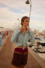 Shorts de cuero marrón con cintura alta de terciopelo burdeos, cordones frontales y apliques de cuero amarillo.