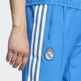 Pantalón deportivo azul con corte ajustado, cintura elástica con cordón ajustable, bolsillos frontales, puños de canalé y escudo del Real Madrid bordado.