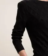 Blusa de manga larga negra confeccionada en punto de viscosa con poliamida e hilos metálicos, con cuello redondo y hombreras. Presenta textura de rayas curvas que forman rombos.