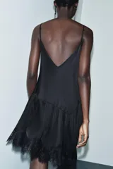 Top negro de tirantes finos con escote pico. Presenta bordados ornamentales en el frente y detalles de puntilla en el escote y el bajo asimétrico.