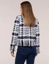 Chaqueta de tweed en blanco y negro con patrón de cuadros, escote redondo, bolsillos frontales con botones metálicos y flecos decorativos en los bordes y puños.