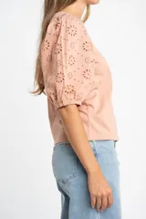 Remera de algodón color rosado con mangas cortas abullonadas de broderie con diseño floral calado. Presenta cuello redondo y costura vertical central en el frente.