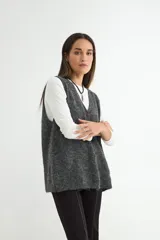 Chaleco tejido de punto en color gris oscuro, con escote en V y cierre frontal de botones marrones. Presenta una textura suave y un corte holgado.