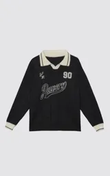 Sweater de punto negro con cuello polo en color crema, manga larga y diseño oversize. Presenta bordados en el frente con la inscripción 'Ravers', el número '90' y letras cursivas, con terminaciones en punto rib en puños y cuello.