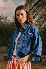 Sobrecamisa de jean de manga corta y corte oversize en color azul medio, con bolsillos frontales con solapa y cierre de botones metálicos a presión.