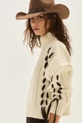 Polera de tejido de punto con diseño de ochos y detalles de tientos en contratono en las mangas. Presenta cuello alto y corte cropped.