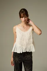 Musculosa negra de breteles finos, confeccionada en algodón con diseño plisado y detalles de encaje. Presenta un corte holgado con volados en el ruedo y escote profundo.