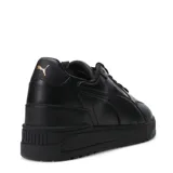 Championes urbanos Puma modelo Shuffle Downtown, color blanco con detalles en negro en la parte trasera y logo dorado en el lateral. Presentan suela de plataforma y cierre con cordones.