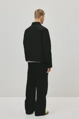 Campera negra de nylon levemente acolchada, con cuello y cierre frontal plateado. Presenta bolsillos insertados al bies y un bolsillo interior con botón a presión. Posee cordón elástico ajustable en el bajo.