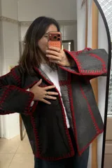 Chaqueta reversible de paño, con un lado gris oscuro con costuras decorativas en hilo rojo y el otro lado con estampado de cuadros. Presenta corte holgado, mangas largas y diseño abierto.