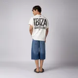Remera oversize color blanco de interlock con sisas al corte, cuello redondo y estampa pequeña frontal con texto en negro.