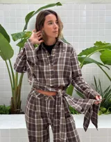 Camisa de manga larga con estampado de cuadros, confeccionada en poliéster. Presenta un diseño versátil con aberturas en las mangas y en el cuerpo que permiten anudar la prenda en la cintura, creando un ajuste personalizado.