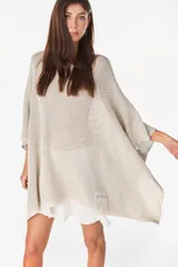 Blusa de punto estilo poncho en color beige, con diseño amplio, cuello redondo y aplique de etiqueta con el logo de la marca en el borde inferior.