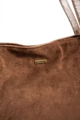 Bolso tipo tote bag color marrón, confeccionado en gamuza vegana con detalles de tiras y asas de hombro en cuero sintético brillante. Incluye una placa metálica pequeña con el logo de la marca en el frente.