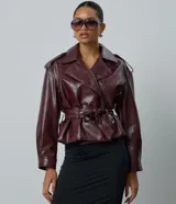 Campera estilo trench coat confeccionada en poliuretano color bordó, con solapas amplias, hombreras decorativas y cinturón ajustable con hebilla en la cintura.