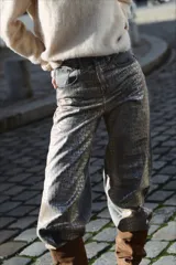 Pantalón de tiro medio con corte baggy y pierna recta. Confeccionado en denim con un proceso de transferencia que le otorga una textura metalizada con efecto de piel de cocodrilo en tonos grisáceos.