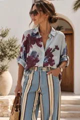 Camisa blanca de manga larga con estampado floral en tonos bordó y verde, cuello camisero, cierre frontal de botones y bolsillos en el pecho con apliques de lentejuelas.
