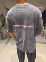 Remera de corte oversize con efecto de lavado ácido en color gris oscuro. Presenta un estampado gráfico en color rosa en la parte posterior con el texto 'BOHEMIAN DSG'.
