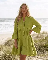 Vestido corto de lino color verde, de corte amplio y diseño escalonado. Presenta cuello mao, escote en V con botones de coco y mangas tres cuartos terminadas con volados.