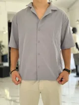 Camisa de lino color beige, de manga corta, con cuello abierto y cierre frontal de botones.