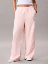 Pantalón de felpa francesa rosa pastel, de corte holgado con basta ancha y tiro medio. Posee cintura elástica, bolsillos laterales y una pequeña insignia blanca con el logotipo de Calvin Klein en el lateral izquierdo.