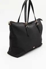 Cartera tipo tote de nylon negro, con diseño amplio y liviano. Presenta asas superiores fijas con detalles de tiras regulables y herrajes metálicos dorados. Incluye cierre principal y un pequeño logo metálico en la parte inferior frontal.