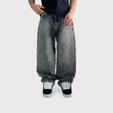 Pantalón de jean estilo baggy con corte oversize, de tiro medio y pierna ancha. Presenta un acabado de lavado ácido en tono gris oscuro y negro, con costuras reforzadas y cierre frontal con botón.