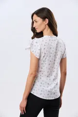 Blusa blanca sin mangas con volados en los hombros, cuello redondo con aberturas y cierre frontal parcial con botones.