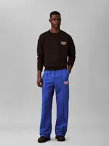 Pantalón de felpa azul con cintura elástica, pierna recta y costuras delanteras decorativas. Cuenta con un pequeño bordado en el muslo.