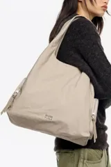 Bolso shopper de nylon color negro, con estructura blanda, doble asa de mano y correa ajustable extraíble. Presenta bolsillos laterales con cierre y logo metálico de la marca en la parte inferior.